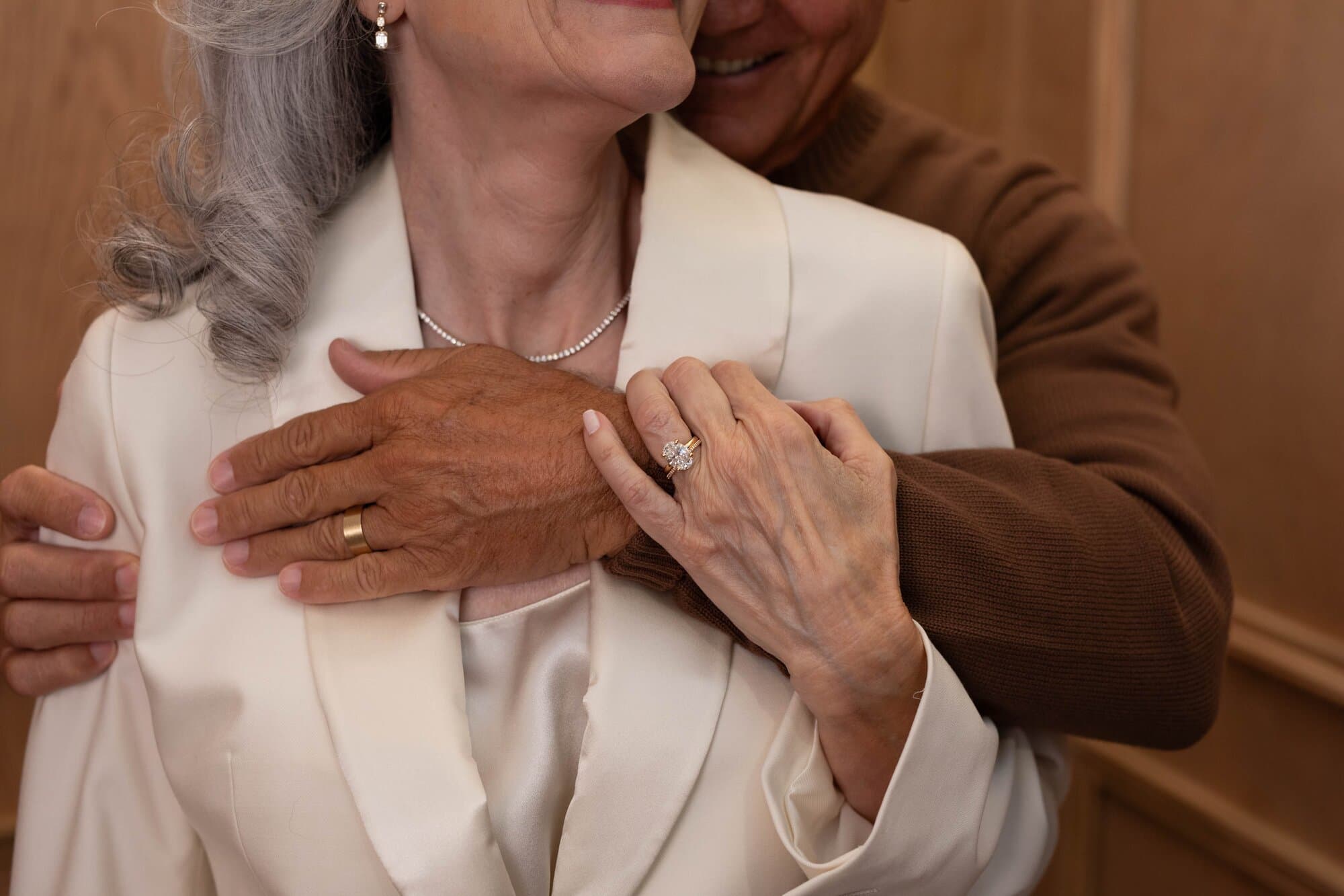 A couple embracing and showcasing their wedding jewelry.