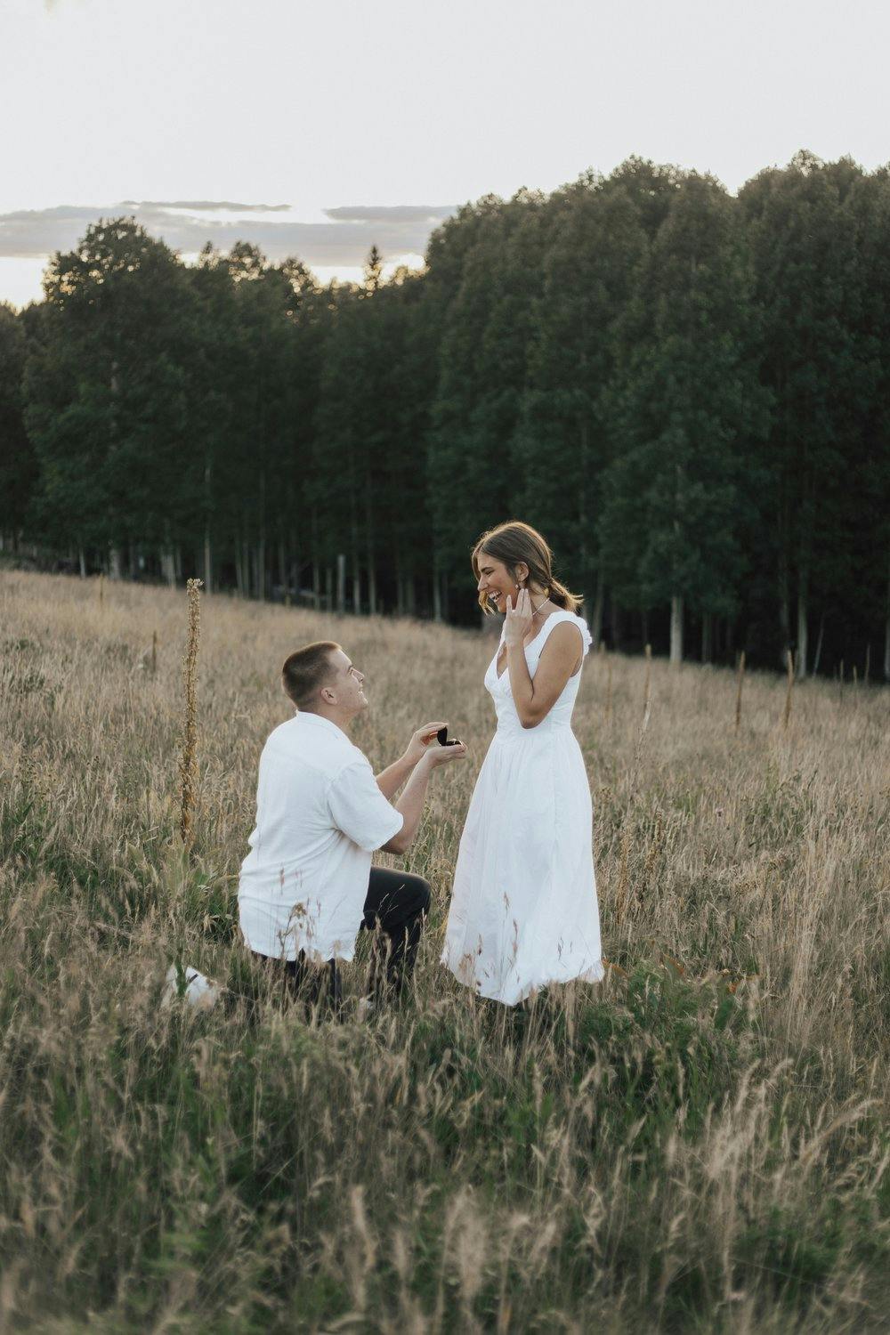a couple in white outfits getting enagaged in a field 
