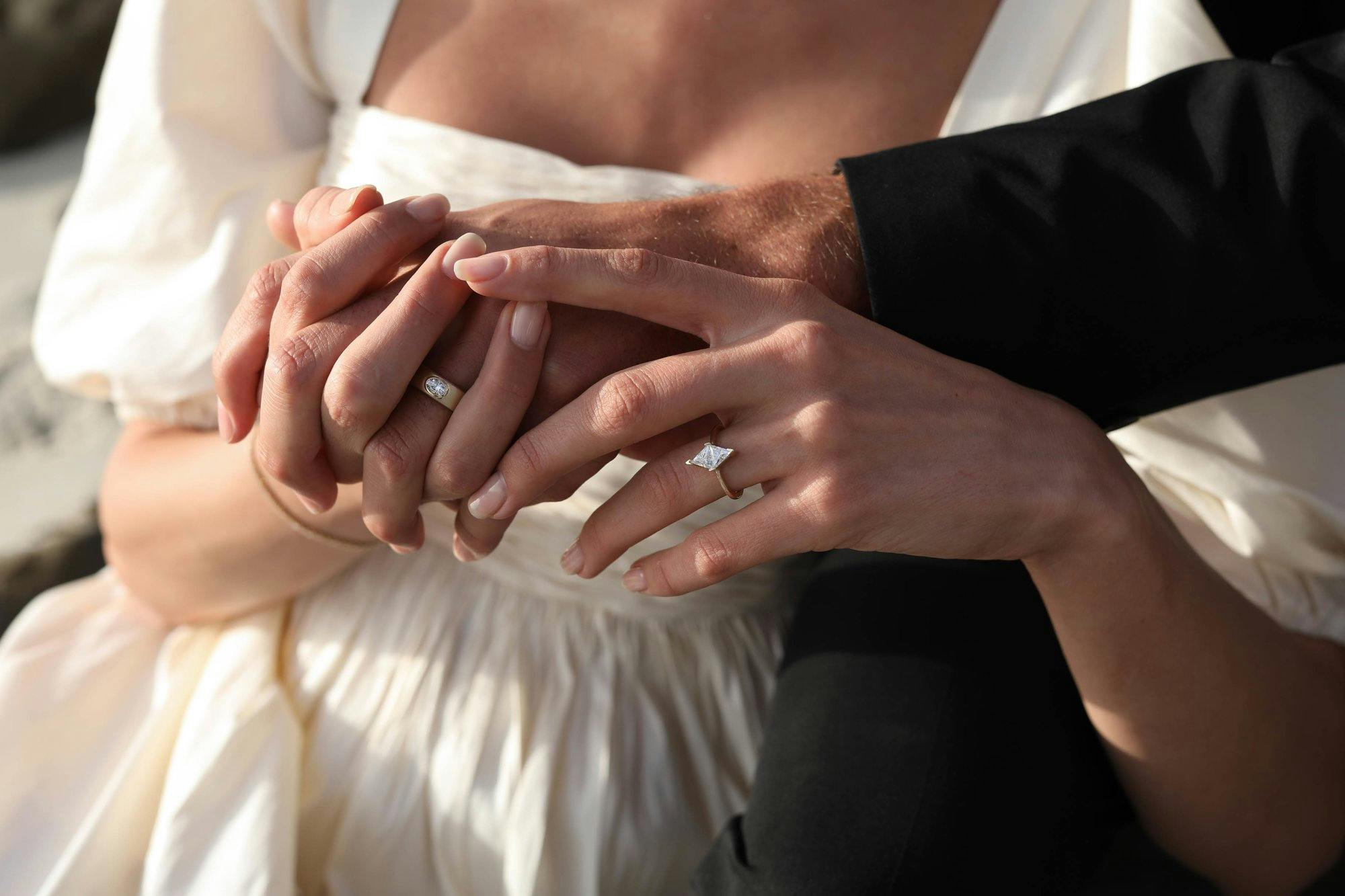 A bride and groom holding hands with an engagement ring in focus