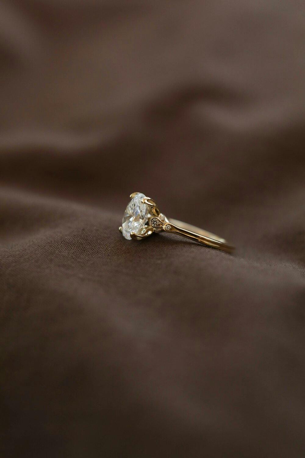 Close up photo of oval, diamond engagement ring with tulip prongs and band detail.