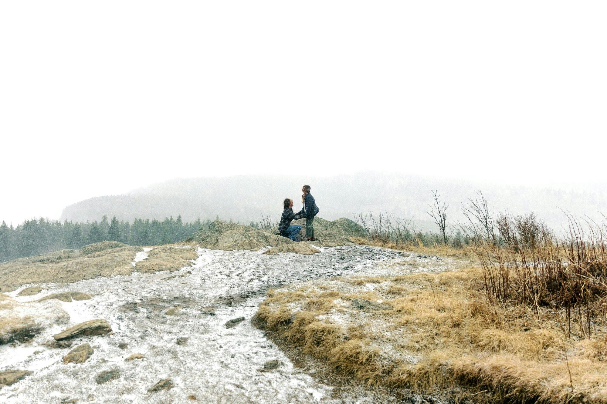 a couple during their proposal on a snowy mountain