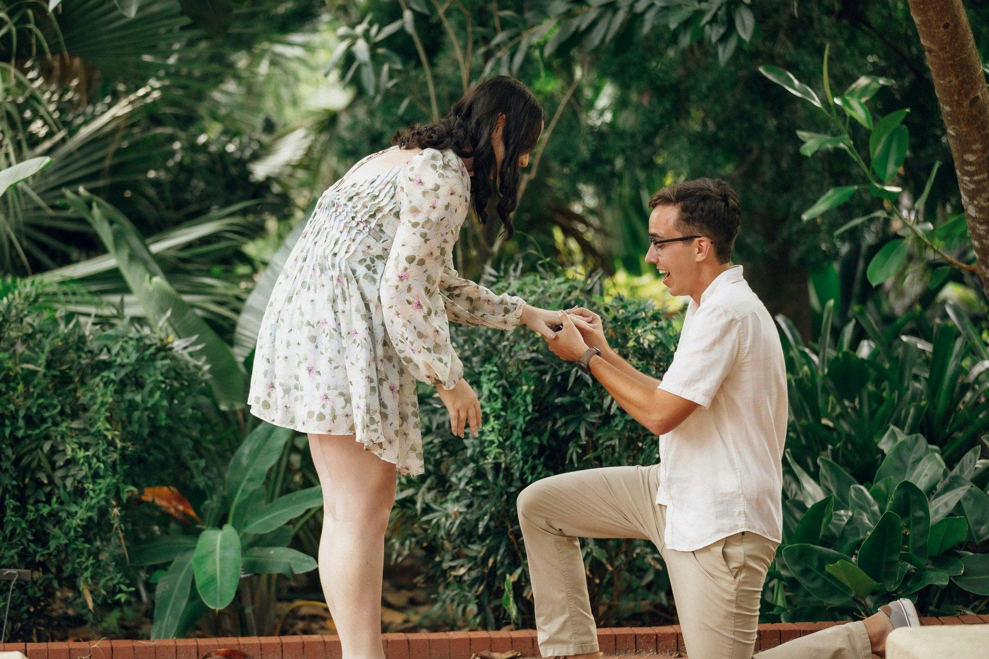 a couple getting engaged in front of greenery