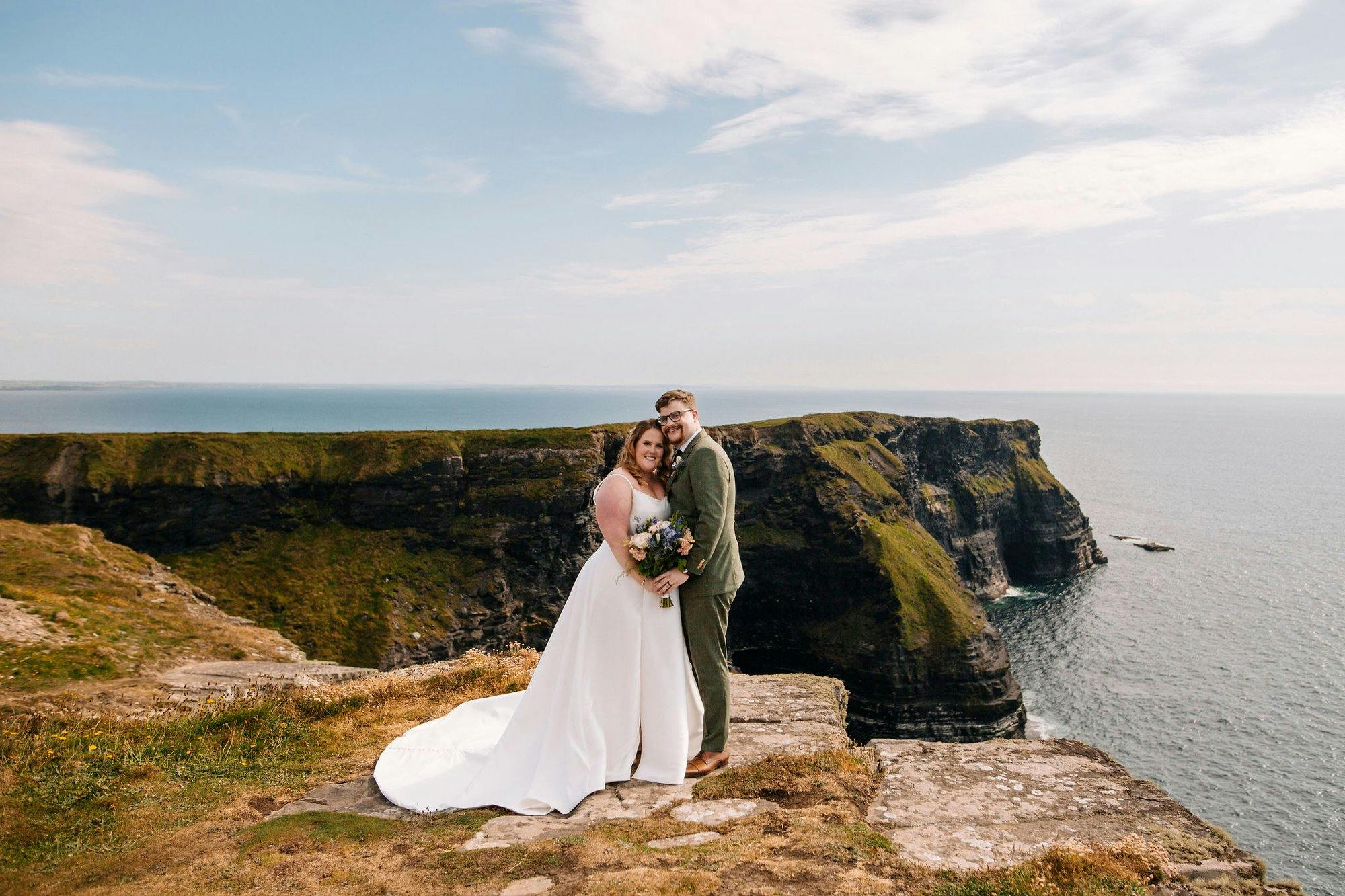 a bride and groom kissing on top of a cliff in Ireland