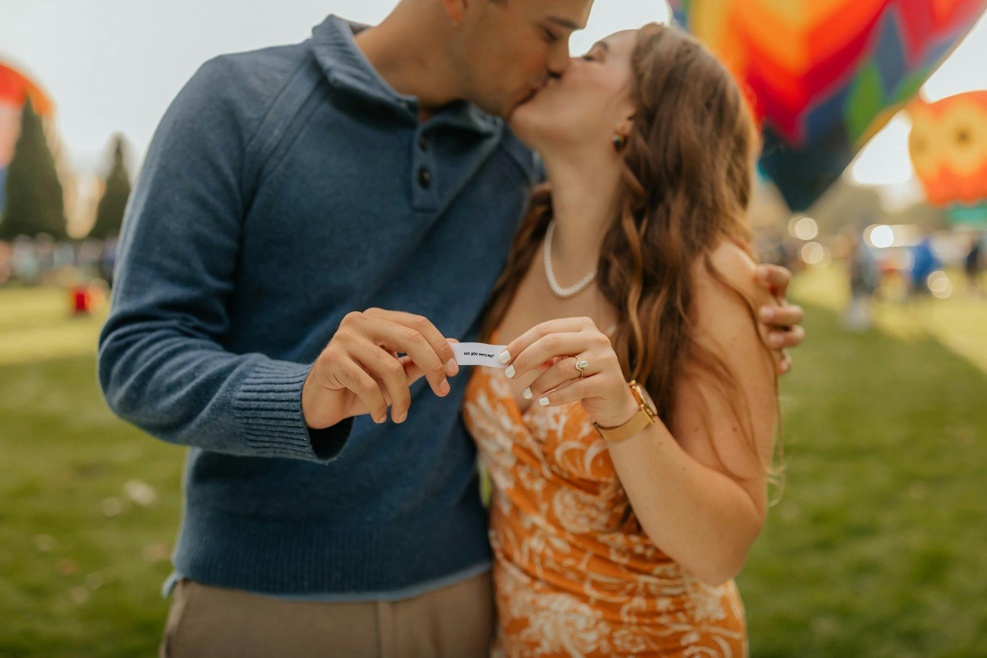 a couple kissing at a hot air balloon festival after their proposal